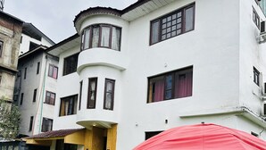 A two-story building with a white facade, a wooden door, and a red umbrella over a table with a checkered tablecloth. - The Iceland Hotel Srinagar (Srinagar)