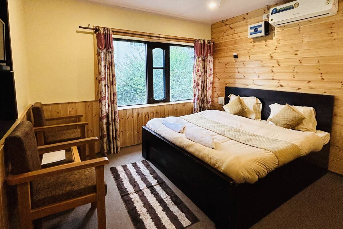 A bedroom with a bed, a desk, a chair, a window with curtains, an air conditioner, and a ceiling fan.