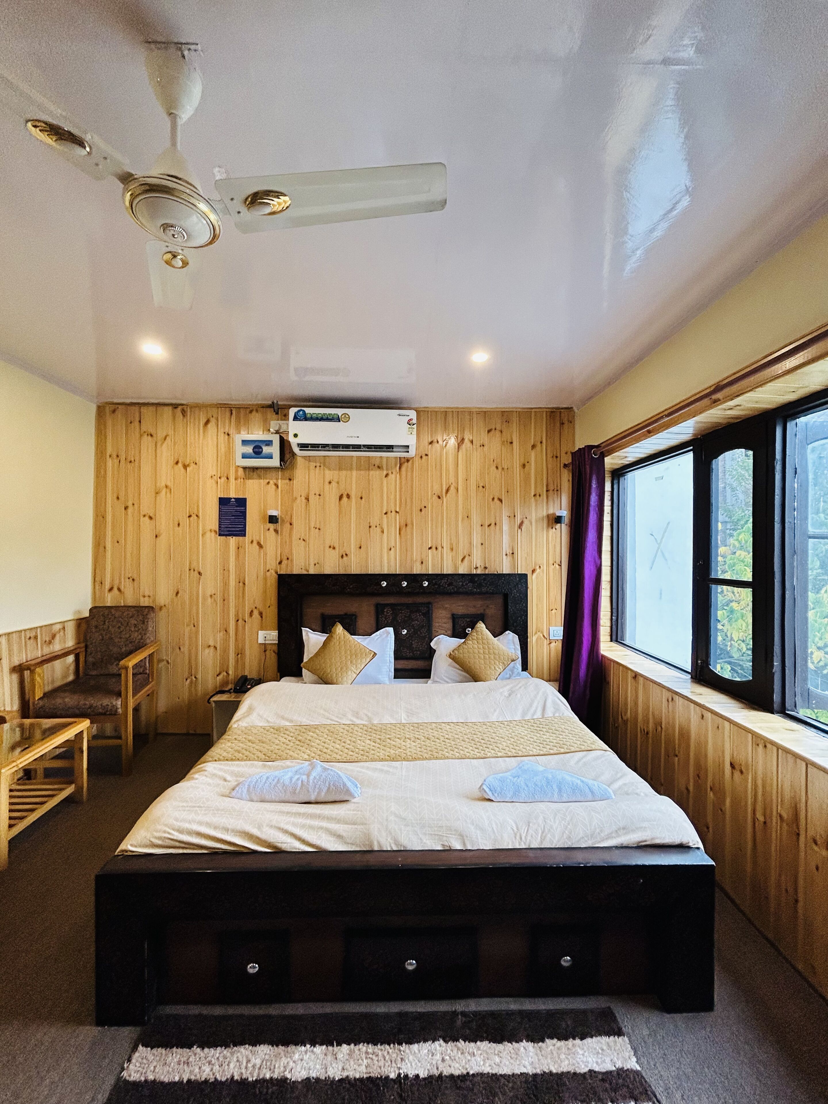 A bedroom with a wooden paneled wall, a bed with white bedding, a ceiling fan, and an air conditioning unit.