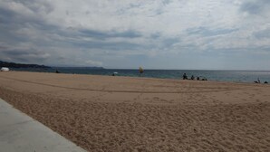 Una playa arenosa y extensa con algunas personas y un paraguas amarillo.
