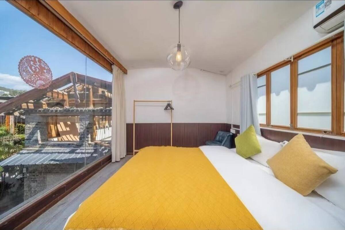 A hotel room with a large bed, a view of a building through a window, and a ceiling light.