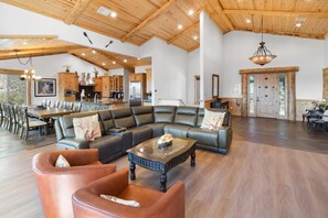 A spacious living area with a sectional sofa, leather armchairs, and a coffee table. - Grand Summit: LUXURY 5000+Sq Ft Log Style Estate! Lake & Sunset Views! HOT TUB! PET FRIENDLY 🐾! Home Theater! Game Room! Central AC! (Big Bear Lake)
