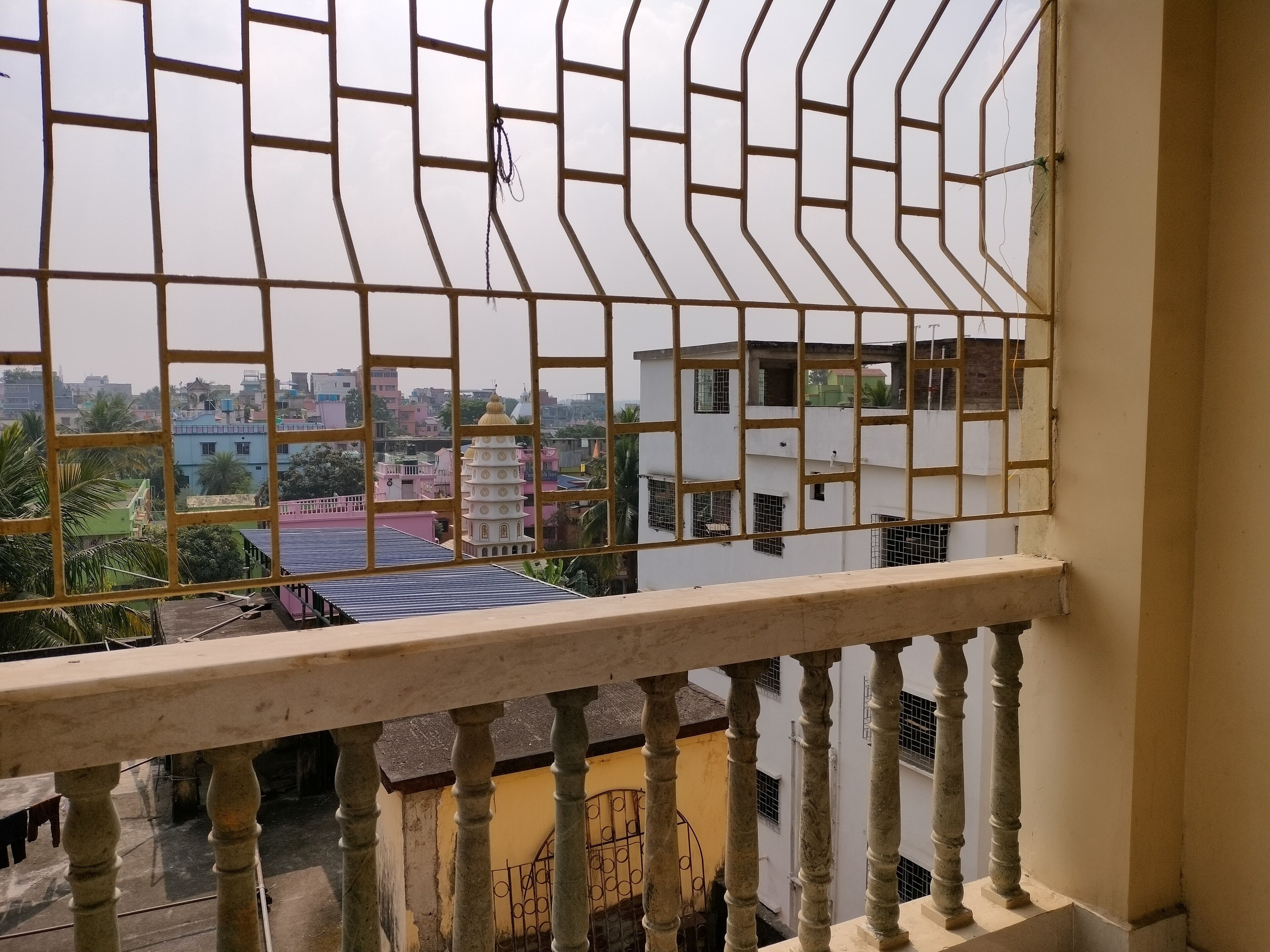 A balcony with a metal railing overlooking a residential area with various buildings and a tower with a dome.