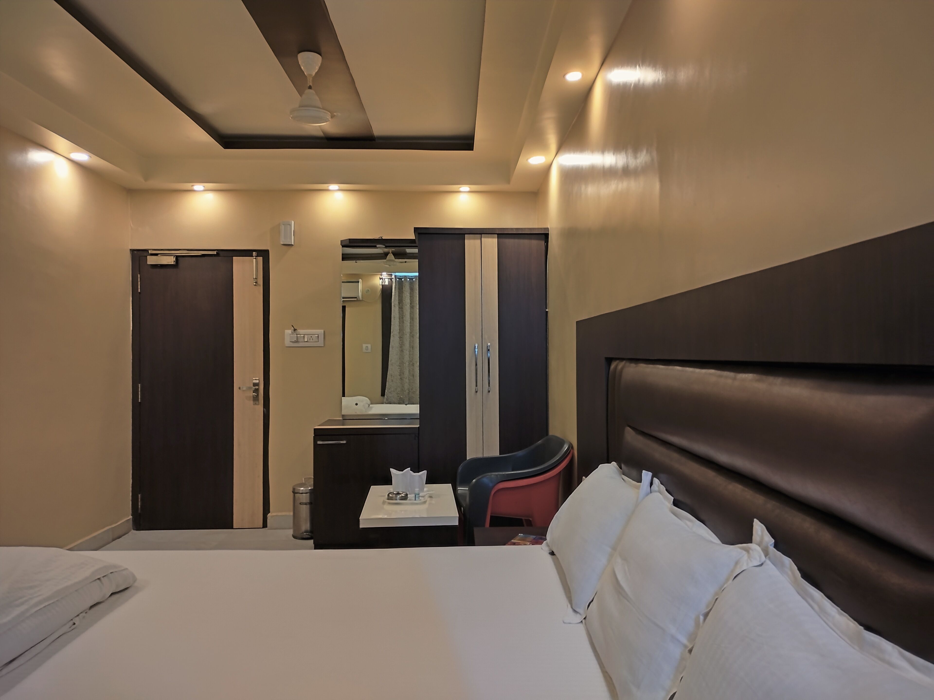 A hotel room with a bed, a desk, a chair, a wardrobe, and a mirror.
