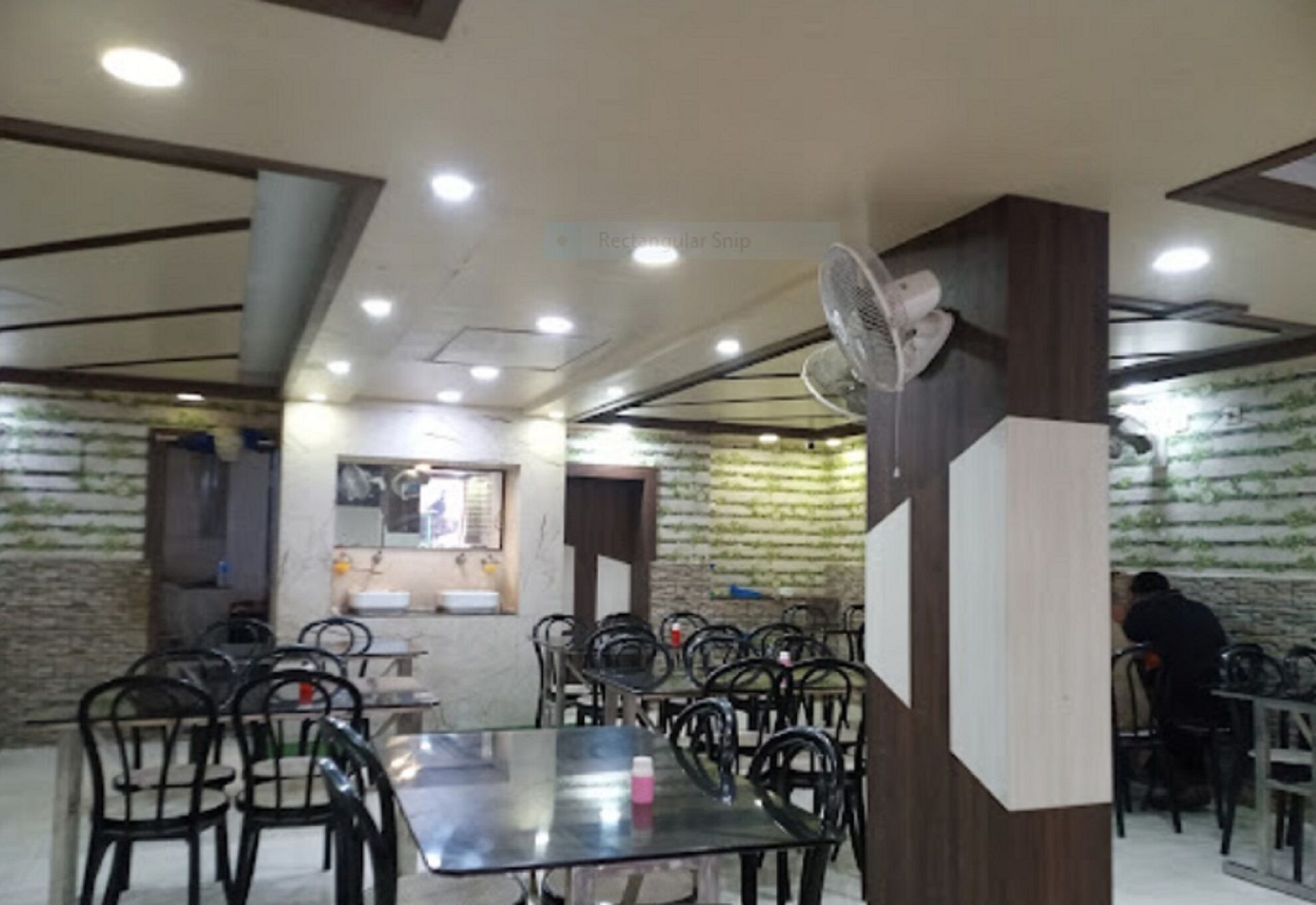 Un restaurante con varias mesas y sillas, un ventilador de techo e iluminación empotrada.