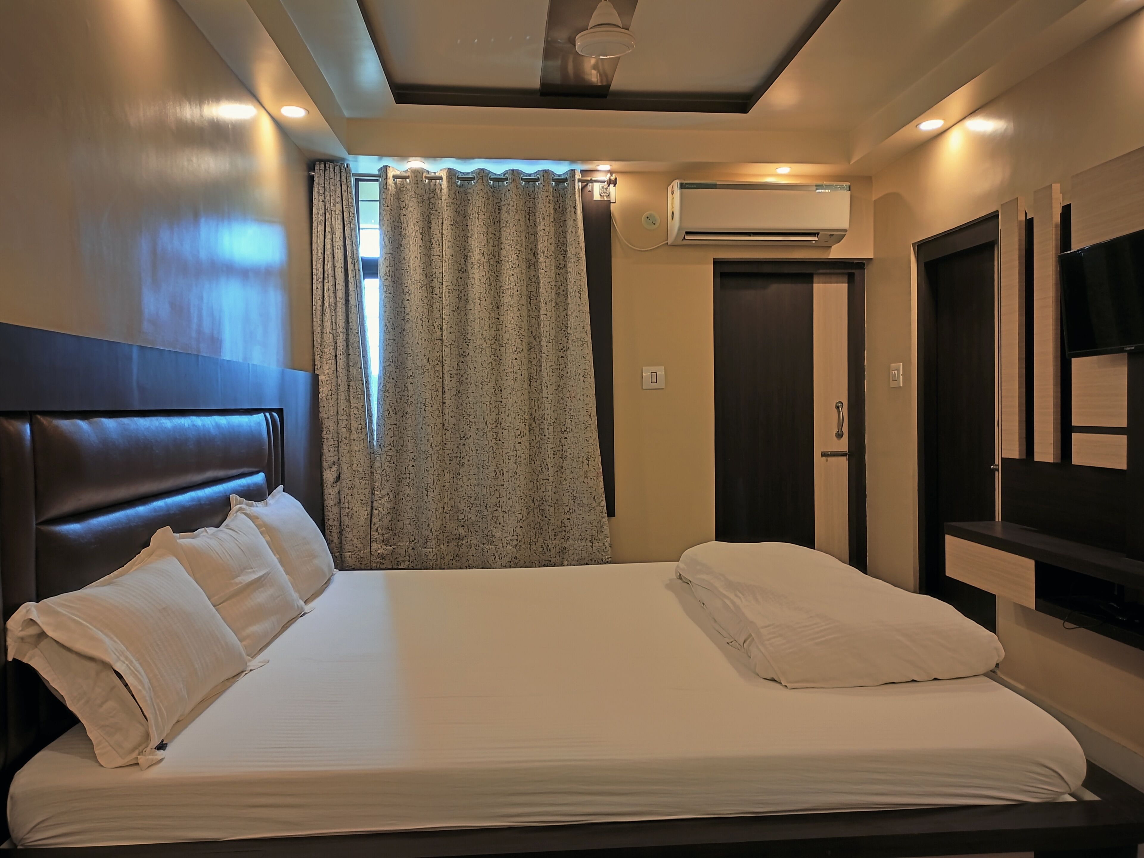 A hotel room with a large bed, an air conditioning unit, a television, and a door.