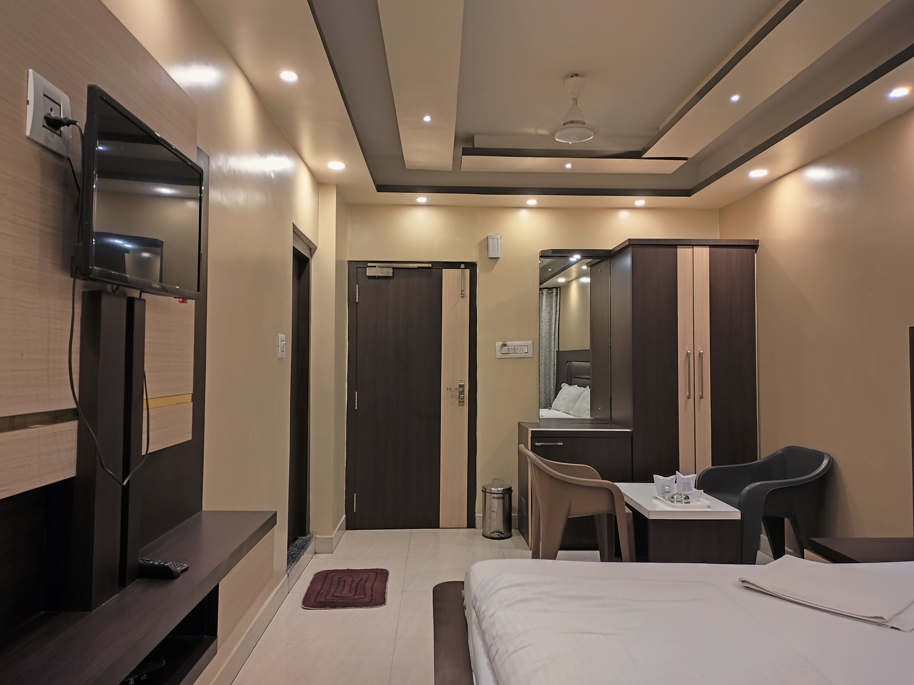 Habitación de hotel con cama, escritorio, silla, televisor montado en la pared y armario.