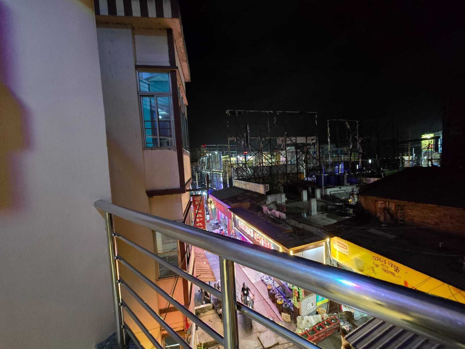 Szenenansicht bei Nacht von einem Balkon mit Geländer, mit Blick auf eine Straße mit Geschäften und Baugerüsten.