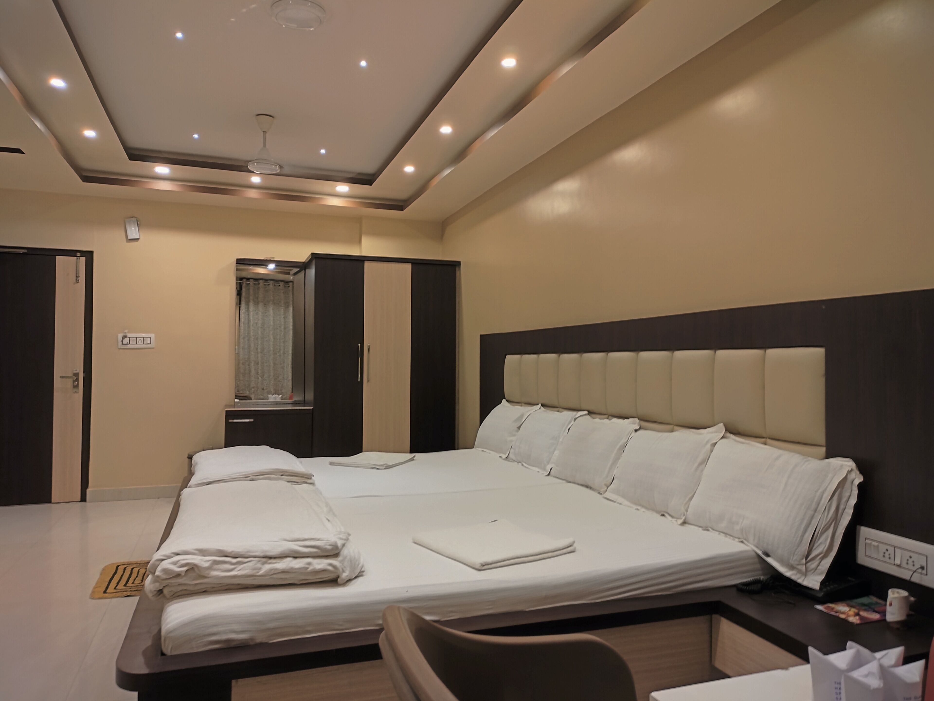 Una habitación de hotel moderna con una cama grande, un armario, una tocador con espejo e iluminación empotrada en el techo.