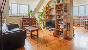 Ein gemütliches Wohnzimmer mit Holzboden, einer schwarzen Ledersofa, einem Holztisch und einem Bücherregal voller Bücher und Dekoration.