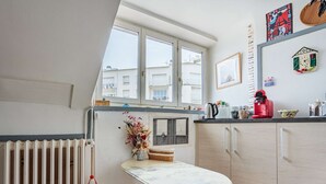 Eine kleine Küche mit Esstisch, zwei Stühlen, Heizkörper und Fenster mit Blick auf Gebäude.