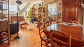 Ein gemütliches Wohnzimmer mit einem Holzesstisch, Stühlen, einem Bücherregal, einem Fernseher und einer Pflanze.