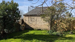 Ein rustikales Steinhaus mit geneigtem Dach, umgeben von einem gepflegten Rasengrundstück und verschiedenen Bäumen.