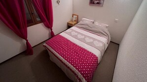 Quarto com cama, mesa de cabeceira, janela com cortinas e luminárias na parede.