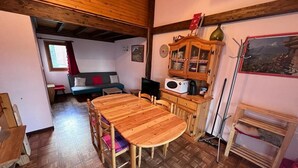 Um quarto aconchegante com uma mesa de jantar de madeira, um sofá e uma cozinha equipada com armários e micro-ondas.