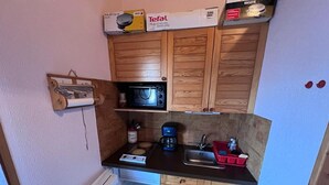 Cozinha compacta com armários de madeira, micro-ondas, cafeteira e uma pia pequena.