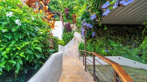 A stone staircase with a wooden handrail leading to a white building surrounded by lush greenery and flowering plants. - Private waterfall, Gated, Near Dominical (Quepos)