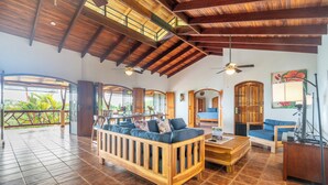 A spacious living area with a wooden sofa, a wooden coffee table, and a desk with a computer. There is a ceiling fan and a painting on the wall. - Private waterfall, Gated, Near Dominical (Quepos)