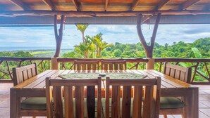 A wooden deck with a table and chairs, overlooking a lush landscape with trees and a distant view of the ocean. - Private waterfall, Gated, Near Dominical (Quepos)