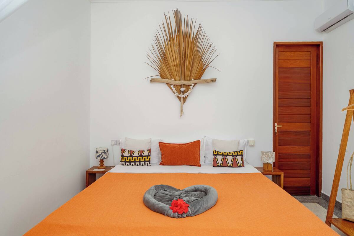 Un dormitorio con cama, un adorno en la pared, una puerta de madera y una mesita de noche con lámpara.