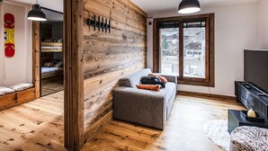 Ett modernt vardagsrum med träväggar, en grå soffa, ett trägolv och ett stort fönster.