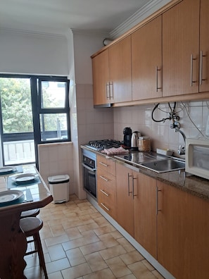 A kitchen with wooden cabinets, a gas stove, a microwave, and a sink. - Largo Frente - Familiar & Acolhedor (Quarteira)