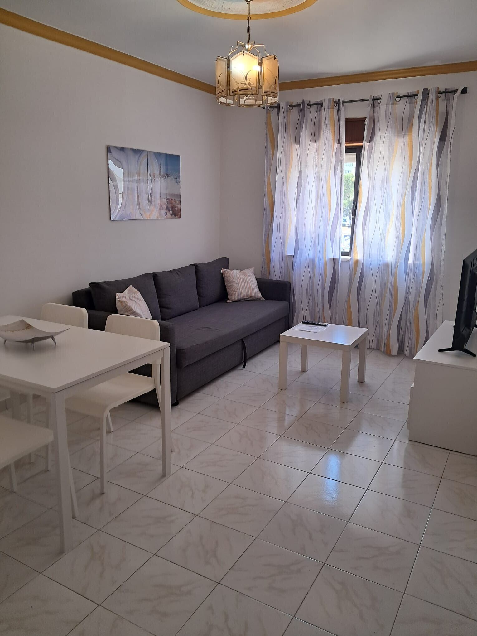 A modern living room with a grey sofa, white coffee table, and a dining table.