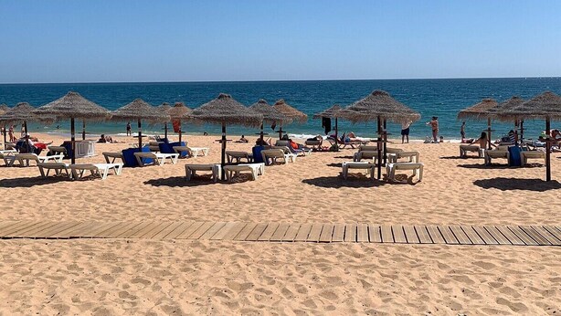 Una playa con tumbonas y sombrillas de paja, un paseo de madera y el océano al fondo.