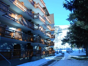 A multi-story hotel with balconies, a snow-covered driveway, and a mountainous backdrop. - Studio at the foot of the slopes with balcony and pets allowed (Les Deux Alpes)