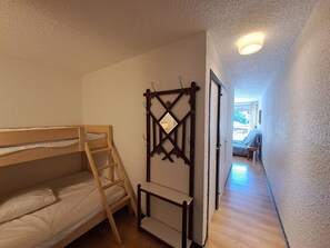 Una habitación con literas, una escalera, una mesita y una puerta que da a otra estancia.