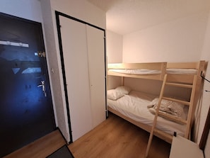Une chambre avec un lit superposé, une porte dotée d’une poignée et un petit bureau.