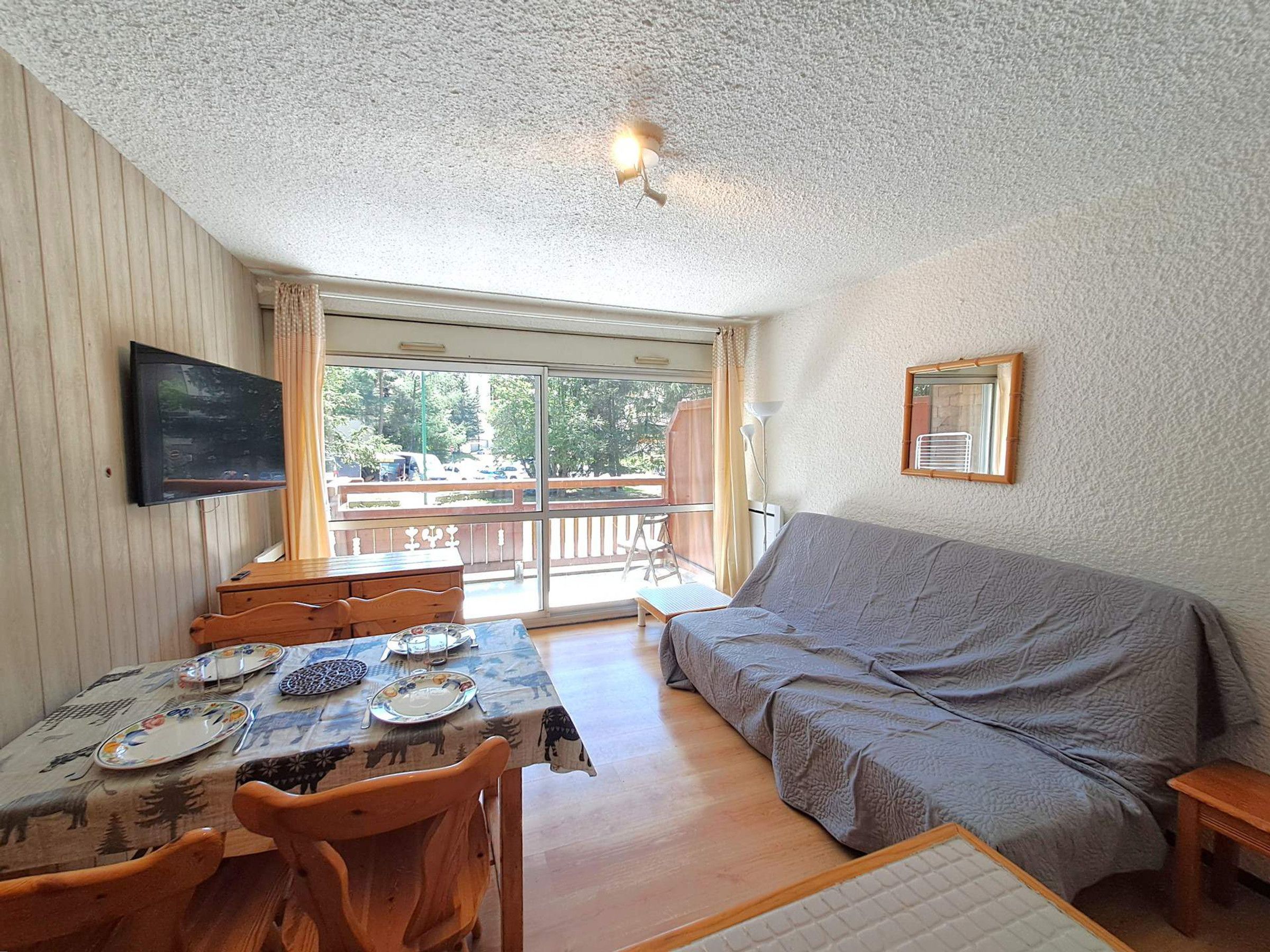 Una habitación con una mesa de comedor, sillas, un sofá, un televisor y un amplio ventanal con vistas al exterior.