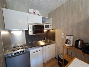 Una cocina compacta con microondas integrado, cafetera y refrigerador pequeño.