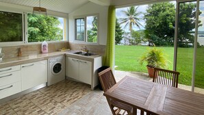 A kitchen with a washing machine, a sink, and a window overlooking a grassy area with trees.