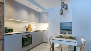 Une cuisine moderne avec des meubles gris, un four encastré, un évier et un coin repas comprenant une table et des chaises.