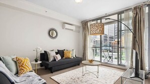 A modern living room with a sofa, a coffee table, and a TV stand. There is a large window with curtains and a view of buildings outside. - A Modern Apt for 6 Right Next to Darling Harbour (Sydney)