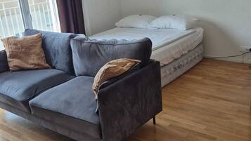 A modern living room with a grey sofa, a mattress, and a wooden floor.