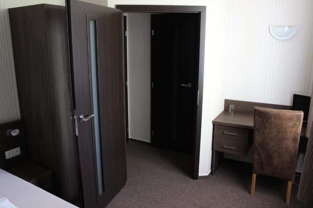 A room with a dark wooden wardrobe, a desk with a chair, and a closed door.