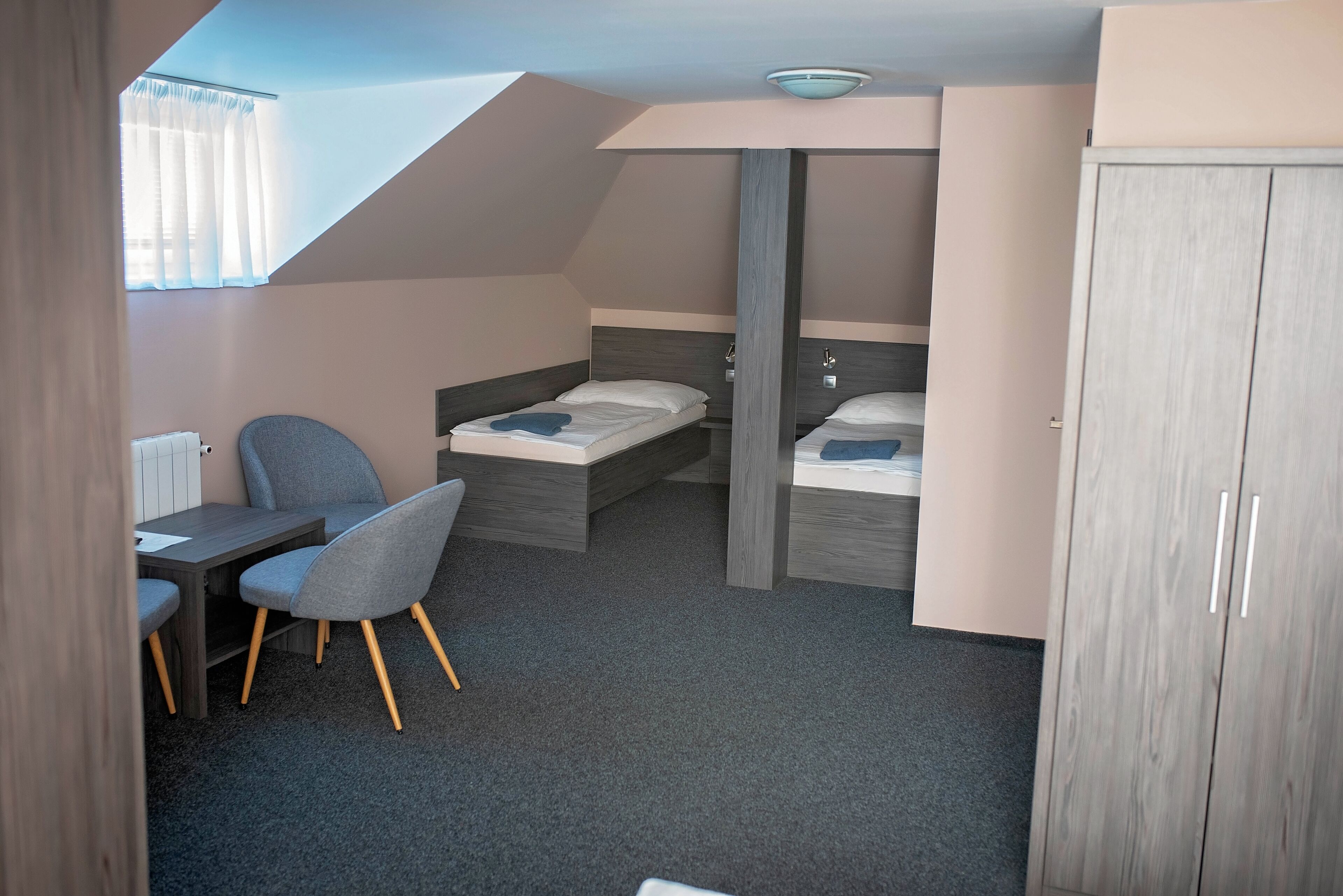 A compact bedroom with two beds, a desk, and a chair.