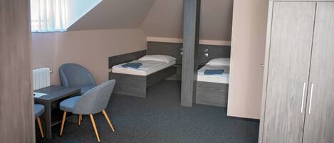 A compact bedroom with two beds, a desk, and a chair.
