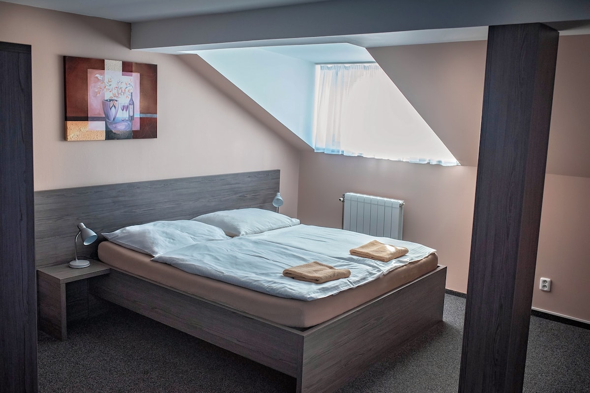 Une chambre moderne avec un plafond en pente, un lit avec des oreillers, une lampe de chevet et un tableau au mur.