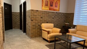 Un vestíbulo con pared de ladrillo, un sofá amarillo, una mesa de centro de vidrio y un cuadro sobre el sofá.