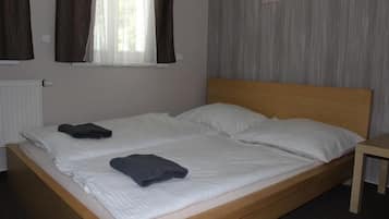Een tweepersoonsbed met witte lakens, een houten hoofdbord en een klein nachtkastje.