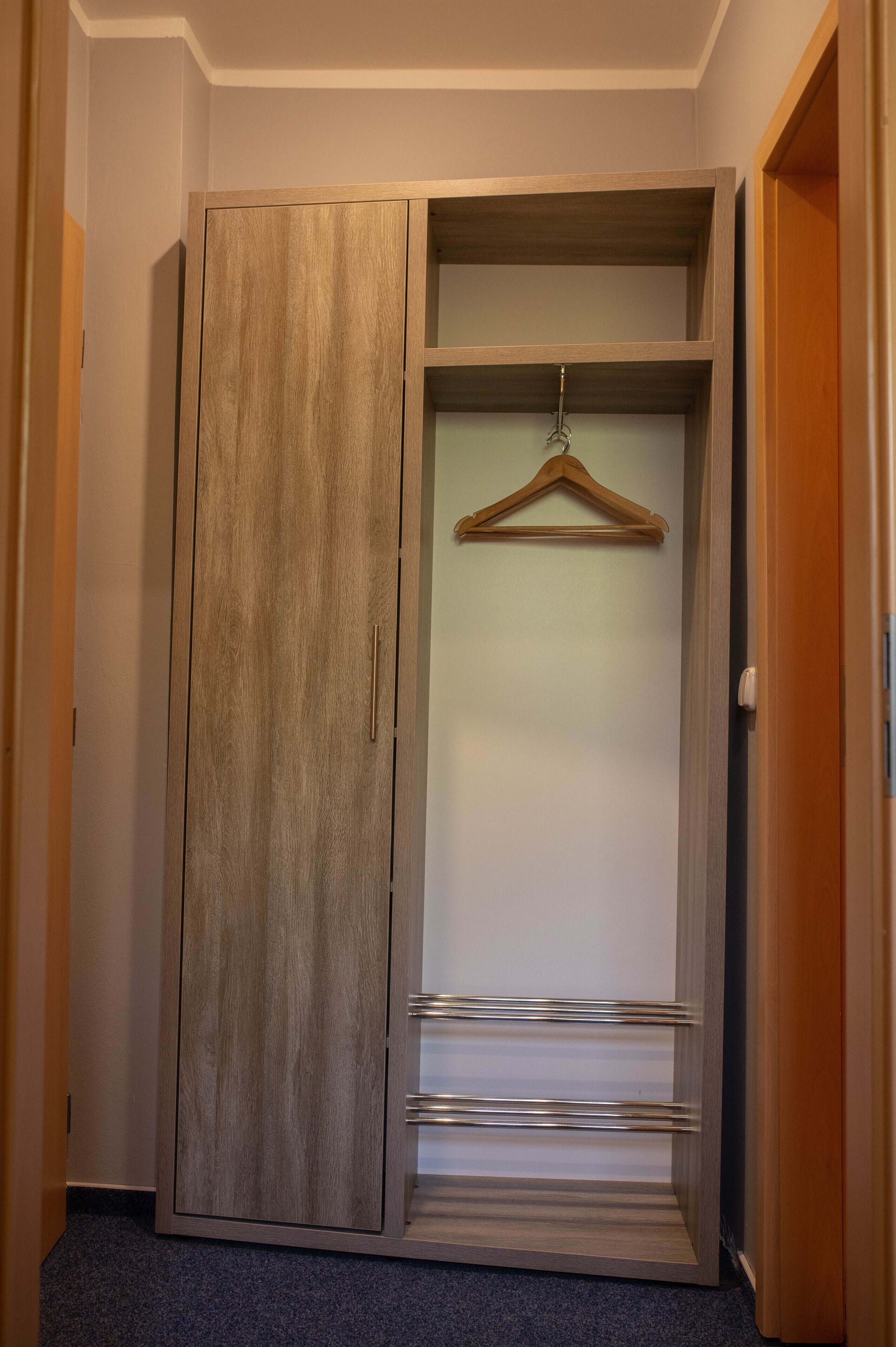 A hallway with a wooden wardrobe, a hanging coat rack, and a door to another room.