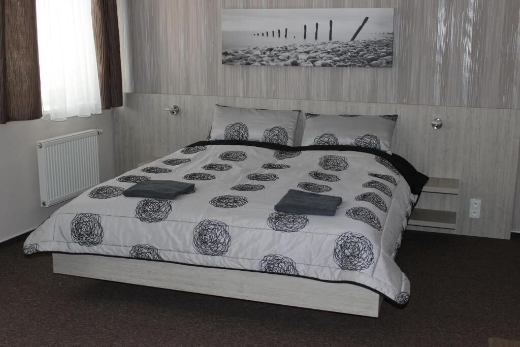 Ein Schlafzimmer mit Bett, Heizkörper, Fenster mit Vorhängen und einem Wandbild.