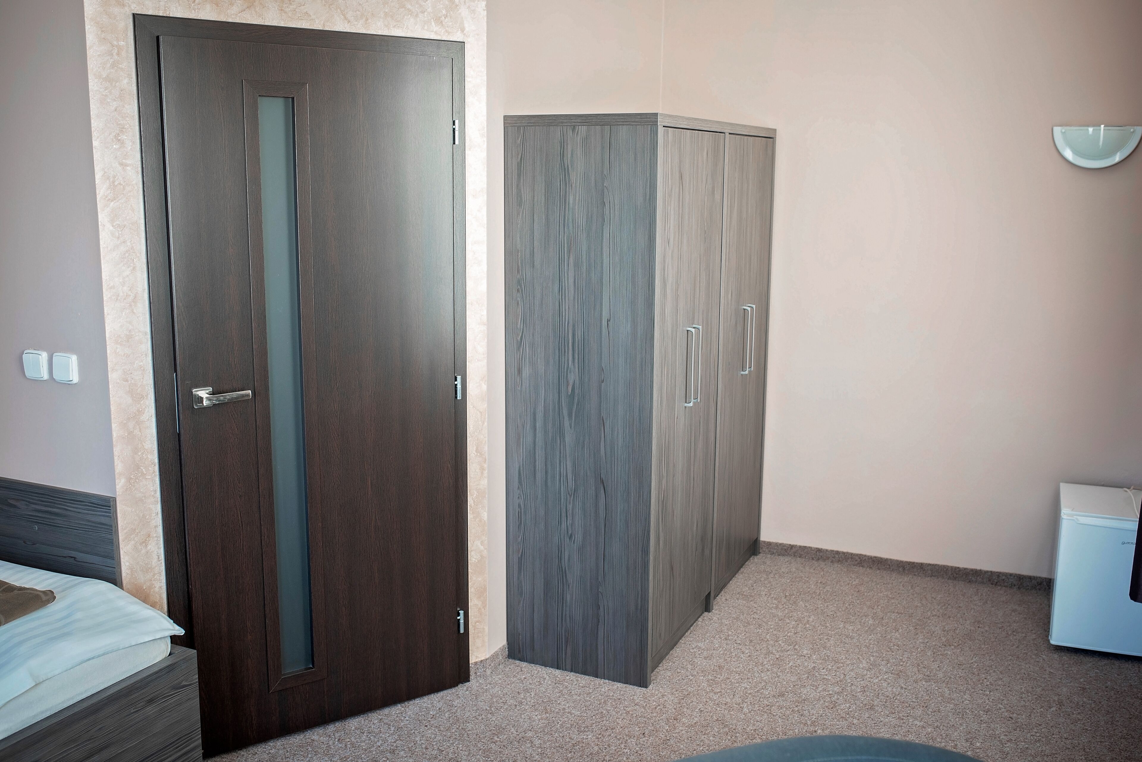 A bedroom with a bed, a wardrobe, and a small white appliance, likely a refrigerator.