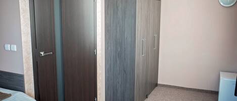 A bedroom with a bed, a wardrobe, and a small white appliance, likely a refrigerator.