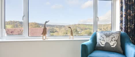 A room with a large window, a blue armchair, and two wooden animal sculptures on the windowsill.