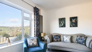 Ein Wohnzimmer mit blauem Sessel, grauem Sofa und Blick auf die Landschaft durch ein großes Fenster.