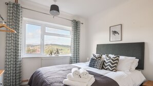 Ein Schlafzimmer mit einem Bett, einem Fenster mit Vorhängen, einem Heizkörper, einem Nachttisch und einem Wandbild.
